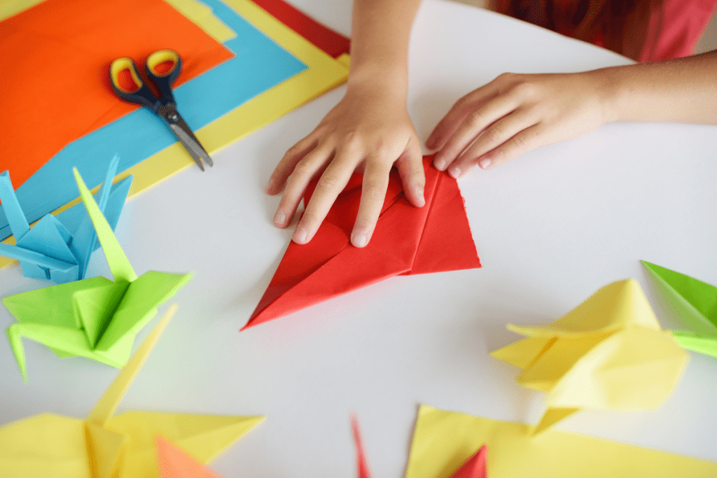 Child hands folding red paper into origami