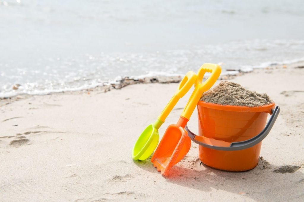 Orange pail filled with sand plus shovels on beach shore