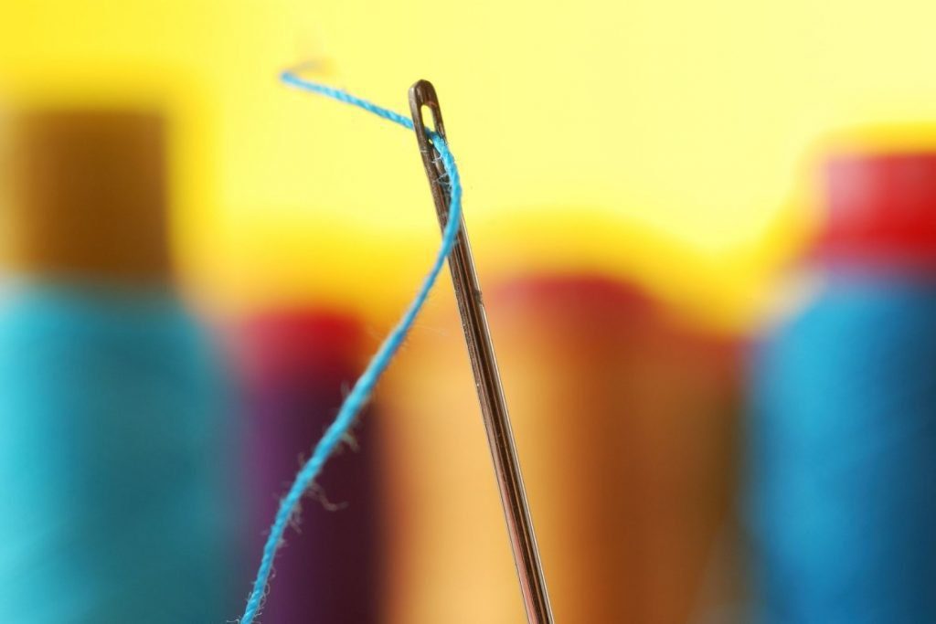 closeup of needle with blue thread on yellow background